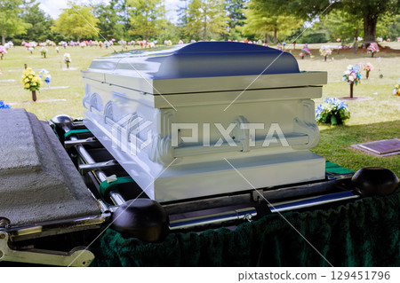 Casket is positioned at gravesite with colorful flowers greenery in peaceful cemetery during memorial service. 129451796