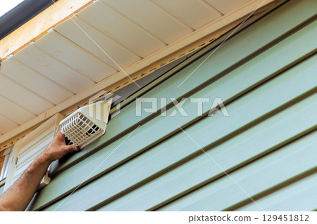 Carpenter is attaching ventilation cover to vinyl side of house, improving airflow home efficiency. 129451812
