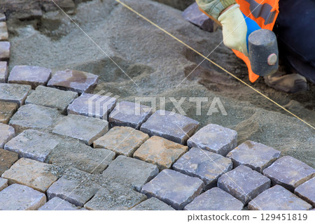 Worker skillfully positions cobblestones while ensuring alignment for new pathway construction 129451819