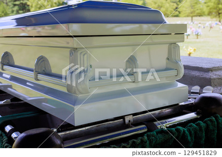 Family gathers at cemetery to pay respects as casket sits on green stand 129451829