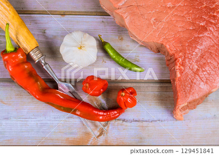 Slices of beef alongside vibrant peppers, garlic on rustic wood table, ready for culinary preparation. 129451841