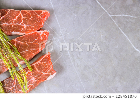 Raw beef steaks garnished with fresh rosemary on smooth marble countertop. 129451876