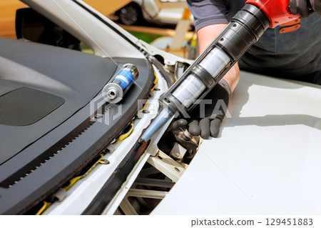 Technician works on car using tool to apply sealant in an auto repair facility during replace windshield 129451883