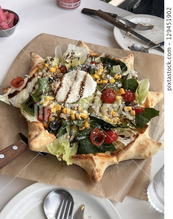 Fresh salad pizza topped with crisp greens, juicy tomatoes, and creamy dressing over a golden crust. A vibrant and healthy twist perfect for casual dining menus and food promotions. 129451902