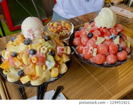 Refreshing gwail bingsu topped with colorful fresh fruits and soft shaved ice, offering a vibrant mix of sweetness and coolness. A perfect summer treat for dessert menus and cafes. 129451921