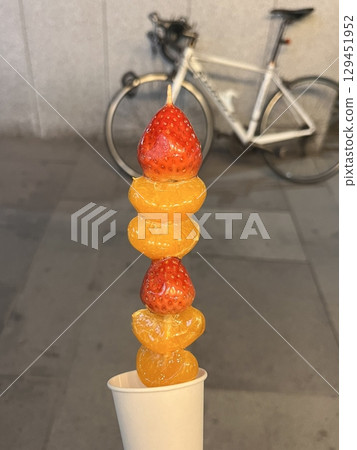 Tanghulu, a traditional Chinese snack made of skewered fruits, usually covered in a shiny sugar coating. Sweet and crunchy, this street food treat is a delightful combination of flavors and textures. 129451952