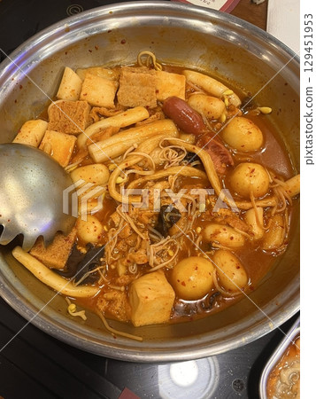 A hearty bowl of Budaejjigae (Korean Army Stew), filled with sausage, tofu, kimchi, and noodles in a spicy broth. This flavorful dish brings warmth and comfort, perfect for sharing. 129451953