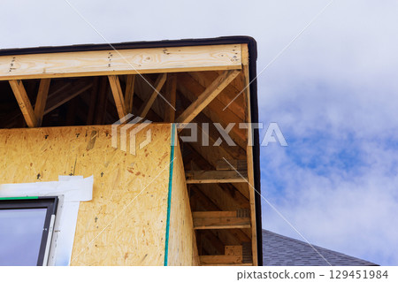 Wooden framing is being constructed on new house with clear blue sky in background. 129451984