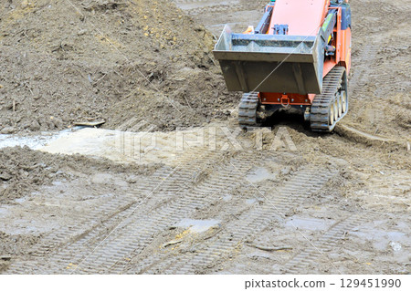 Heavy machinery operates on muddy construction site, shifting dirt preparing area for development. Heavy machinery operates on muddy construction site, shifting dirt preparing area for development. 129451990