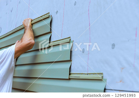 Construction worker carefully places installing new pvc vinyl siding siding panels on building exterior wall Construction worker carefully places installing new pvc vinyl siding siding panels on building exterior wall 129451993
