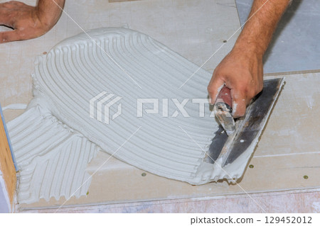 Skilled hands apply adhesive on subfloor in preparation for new flooring installation during home renovations. 129452012