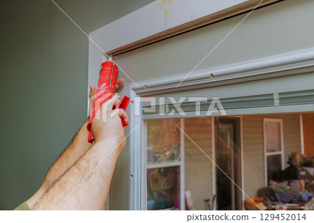 Carpenter is using caulk gun to seal gaps around door frame in home improvement effort. 129452014