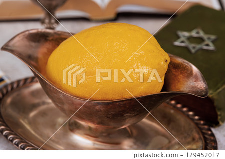 Traditional Jewish holiday etrog fruit with religious books. Sukkot celebration symbols with Star of David 129452017
