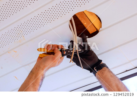 An electrician expertly connects wires through ceiling opening, demonstrating skill attention to detail. An electrician expertly connects wires through ceiling opening, demonstrating skill attention to detail. 129452019