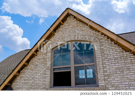Gable of brick house featuring large windows highlighting architectural details on works day. 129452025