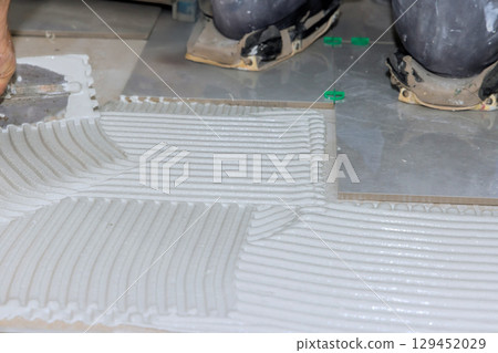 Construction workers apply adhesive on floor for tile installation in bright work area. 129452029