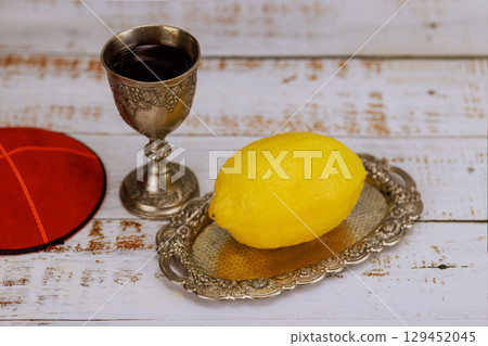 Traditional Jewish ceremonial, etrog citrus fruit rests on kiddush cup filled with wine yarmulke visible for Jewish holidays like Sukkot. 129452045