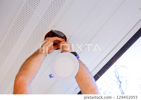 Homeowner works diligently to install new ceiling light fixture in their living room during works day Homeowner works diligently to install new ceiling light fixture in their living room during works day 129452055