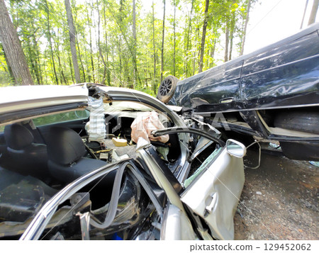 Two heavily damaged cars are seen entangled in collision in forested area under bright daylight. 129452062