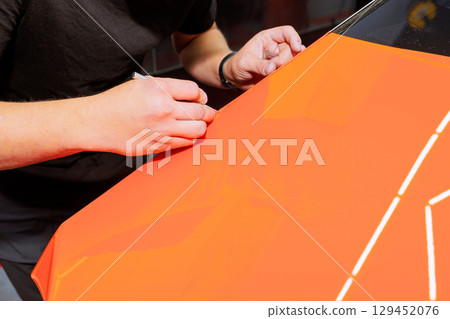 Worker is meticulously on bright orange surface, showcasing artistic skill in car service environment. Worker is meticulously on bright orange surface, showcasing artistic skill in car service environment. 129452076
