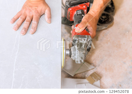Craftsman polishing tile stone surface with power tool, showcasing expertise in workshop environment. Craftsman polishing tile stone surface with power tool, showcasing expertise in workshop environment. 129452078