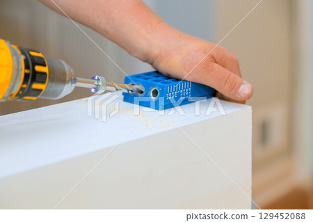 Carpenter drills into wood using guide for precise positioning in craft space. 129452088