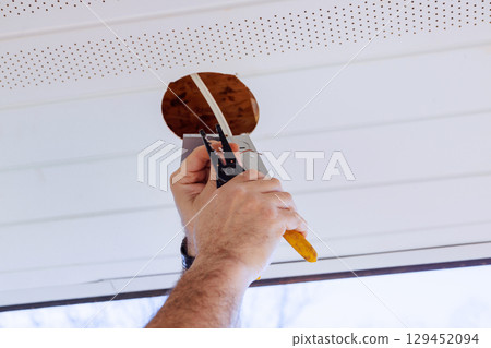 Electrical uses tools to install ceiling light fixture in home while natural light fills space. 129452094