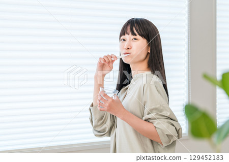 Young Asian, Japanese woman brushing her teeth with a toothbrush at home (dental care) 129452183