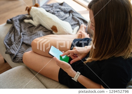 Woman using smartphone while relaxing at home with dog 129452796