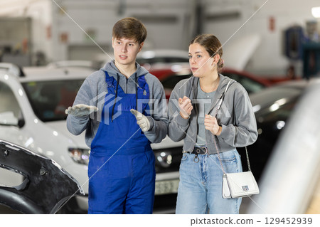 Young man car mechanic talks with girl client in workshop and takes order. Young man car mechanic talks with girl client in workshop and takes order. 129452939