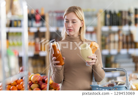 Girl buyer examine good, doubt and choose between varieties sauce in store Girl buyer examine good, doubt and choose between varieties sauce in store 129453069
