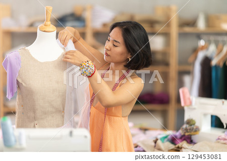 Female tailor sews new dress on a mannequin in sewing studio 129453081