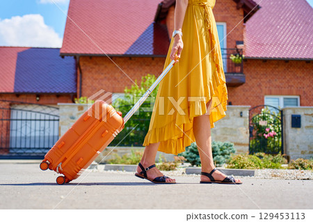 Woman walking with orange suitcase outdoors Woman walking with orange suitcase outdoors 129453113