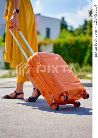 Woman walking with orange suitcase outdoors Woman walking with orange suitcase outdoors 129453114