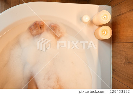 Person relaxing in bubble bath with candles 129453132