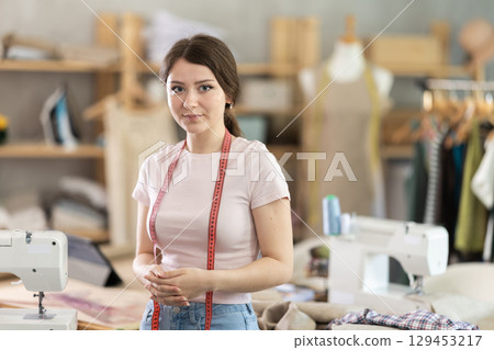 Portrait of positive girl tailor in sewing workshop 129453217