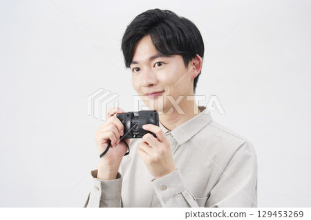 A man in his 20s holding a film camera on a white background 129453269