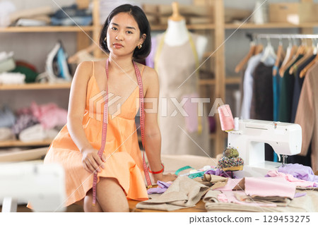 Portrait of positive girl tailor in sewing workshop Portrait of positive girl tailor in sewing workshop 129453275