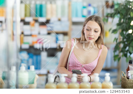 Woman in summer dress with phone in hands in pharmacy 129453543
