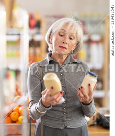 Elderly woman choosing mayonnaise in grocery store 129453545