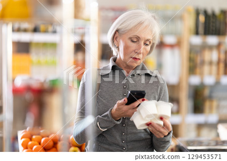 Checking expiration date of yogurt - elderly female shopper scans QR code on label of yogurt using smartphone 129453571