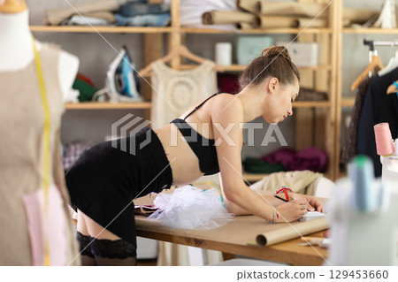 Young woman in stockings drawing pattern on paper Young woman in stockings drawing pattern on paper 129453660