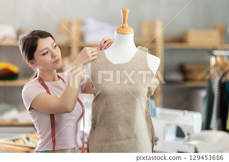 Woman seamstress adjusts clothes on mannequin 129453686