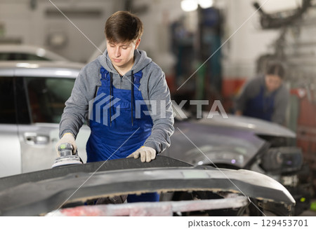 Young man auto mechanic polishes body parts by car buffer polisher machine tool 129453701