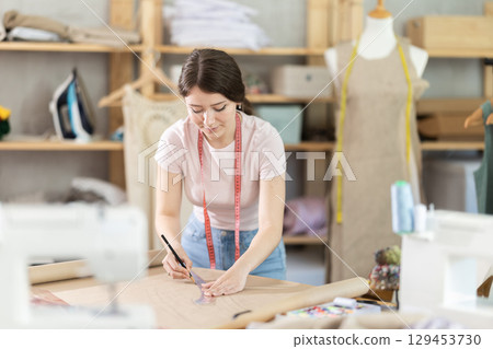 Woman dressmaker drawing pattern on paper in workshop 129453730