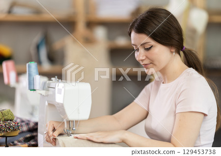 Woman seamstress sews on sewing machine in workshop Woman seamstress sews on sewing machine in workshop 129453738