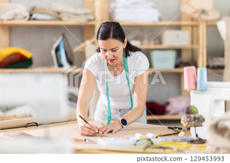 Woman dressmaker drawing pattern on paper in workshop 129453993
