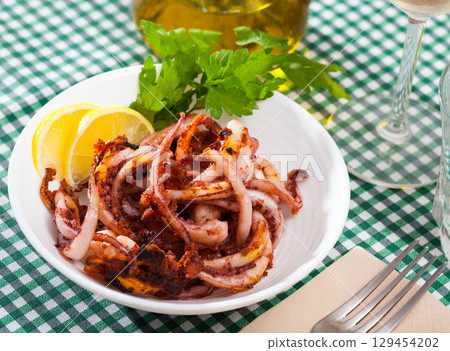 Delicious cooked squid or octopus tentacles with lemon and parsley on a plate Delicious cooked squid or octopus tentacles with lemon and parsley on a plate 129454202