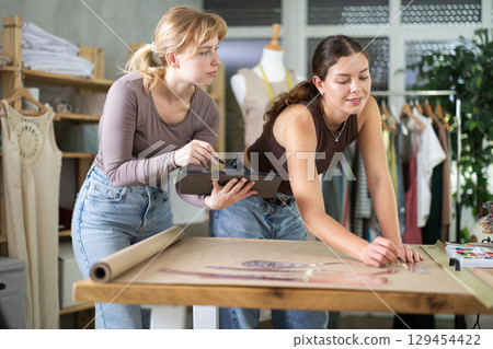 Female tailors working together in workshop with tablet and paper 129454422