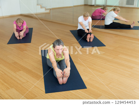 Women practicing yoga, sitting in Seated forward bend exercise, paschimottanasana pose 129454453